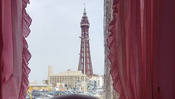 A bed with a plaid bedspread, curtains framing a view of a building with a tower. - Gracelands Guest House (Blackpool)