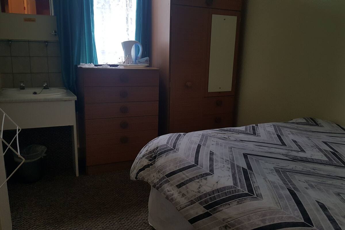 Une chambre à coucher avec un lit, une commode, un lavabo et une fenêtre avec des rideaux.