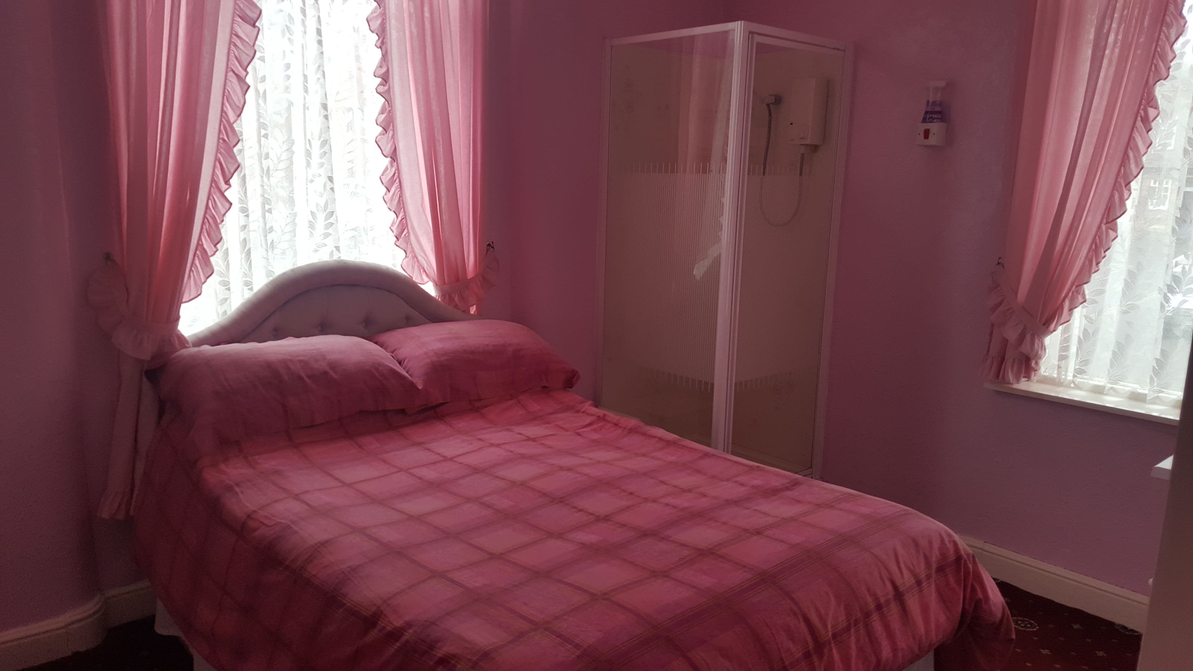 A bedroom with a bed, pink curtains, a wardrobe, and a window.