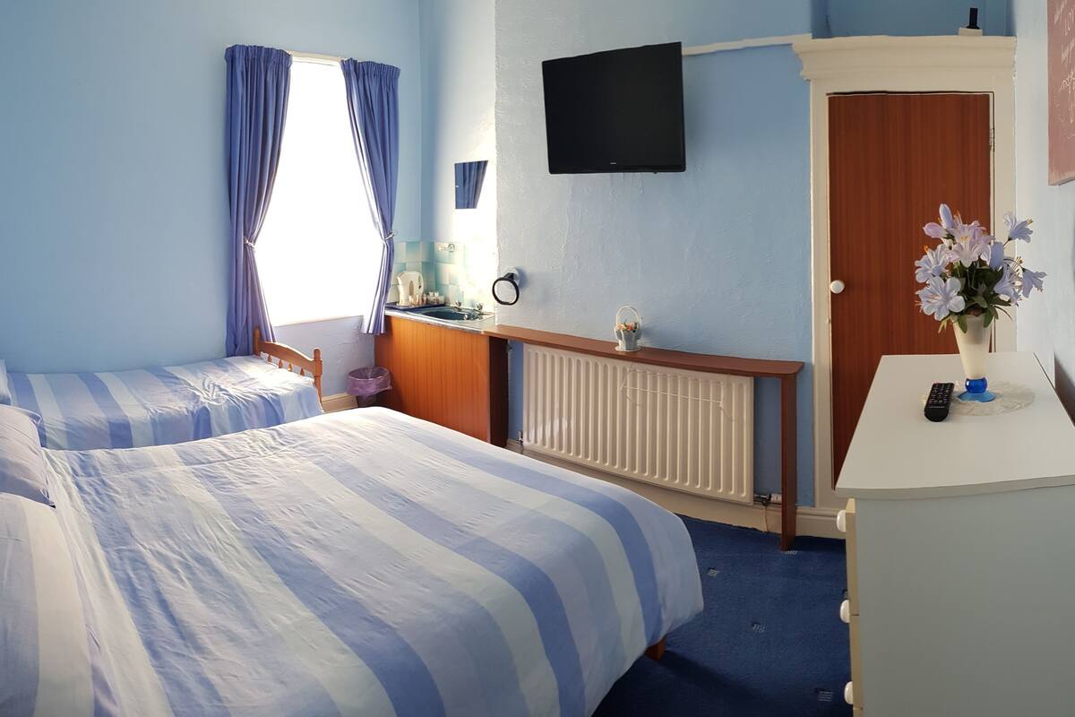 Une chambre avec deux lits, une télévision, un bureau et un radiateur.