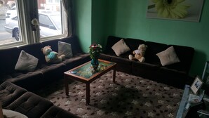 A living room with a sofa, a coffee table, and a window with a view of a car outside. - Gracelands Guest House (Blackpool)