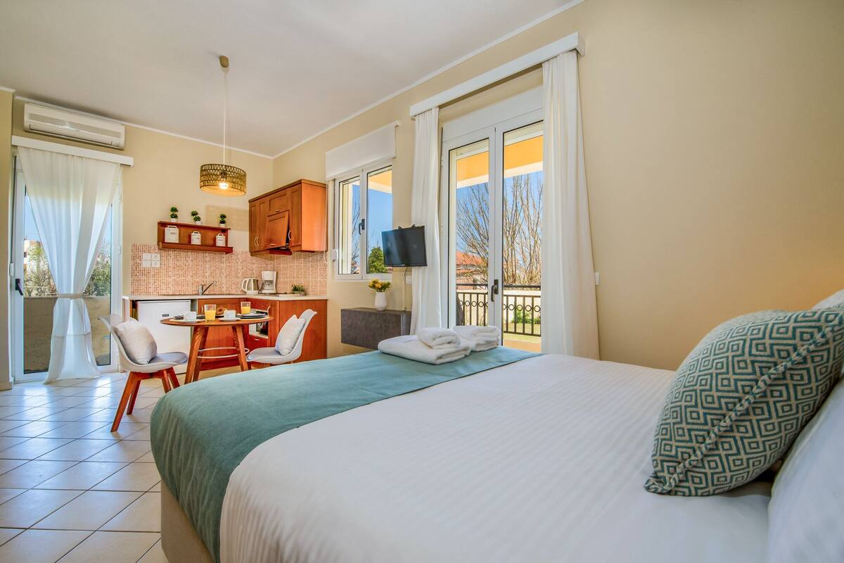 A hotel room with a bed, a desk, a chair, a TV, and a balcony with a view.