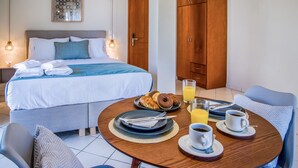 A hotel room with a neatly made bed, breakfast table with croissants, coffee, and orange juice, and a large wardrobe. - Gianthea Studios and Apt (Chania)
