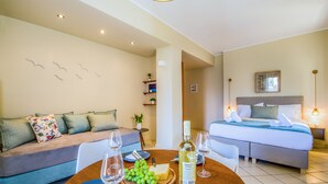 A modern hotel room with a sofa, a bed, a dining table set with a bottle of wine, grapes, and a cheese board. - Gianthea Studios and Apt (Chania)