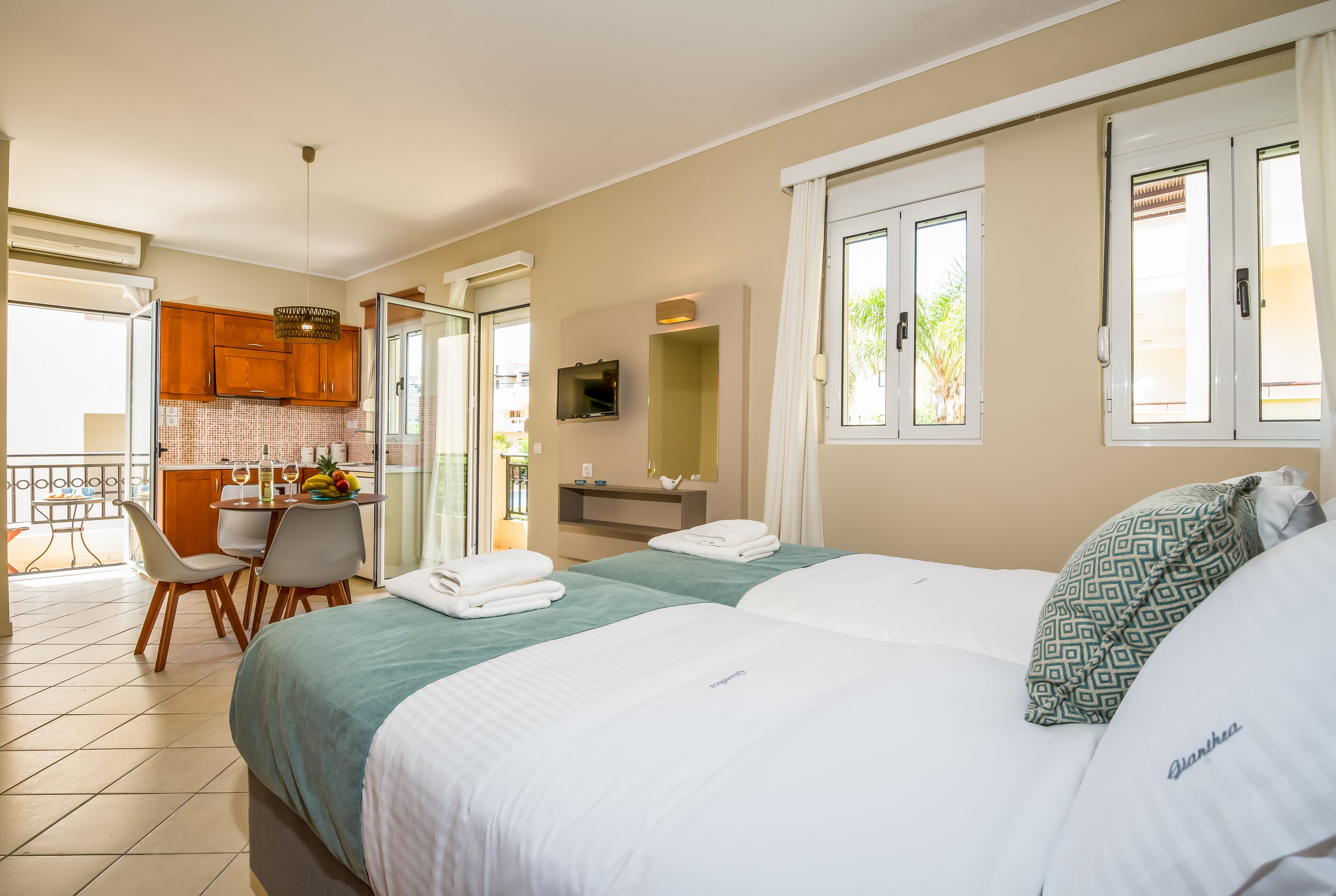 A hotel room with a bed, a desk, a chair, a small kitchen area, and a balcony.