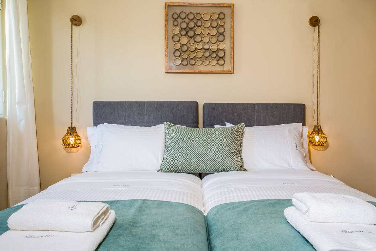 A neatly made double bed with a green and white patterned pillow, two bedside lamps, and a framed artwork above.