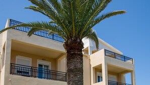 A two-story building with balconies, a palm tree, and a paved walkway. - Gianthea Studios and Apt (Chania)