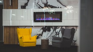 A modern living room with a fireplace, two chairs, and a marble wall. - Quality Hotel & Conference Centre (Edmundston)