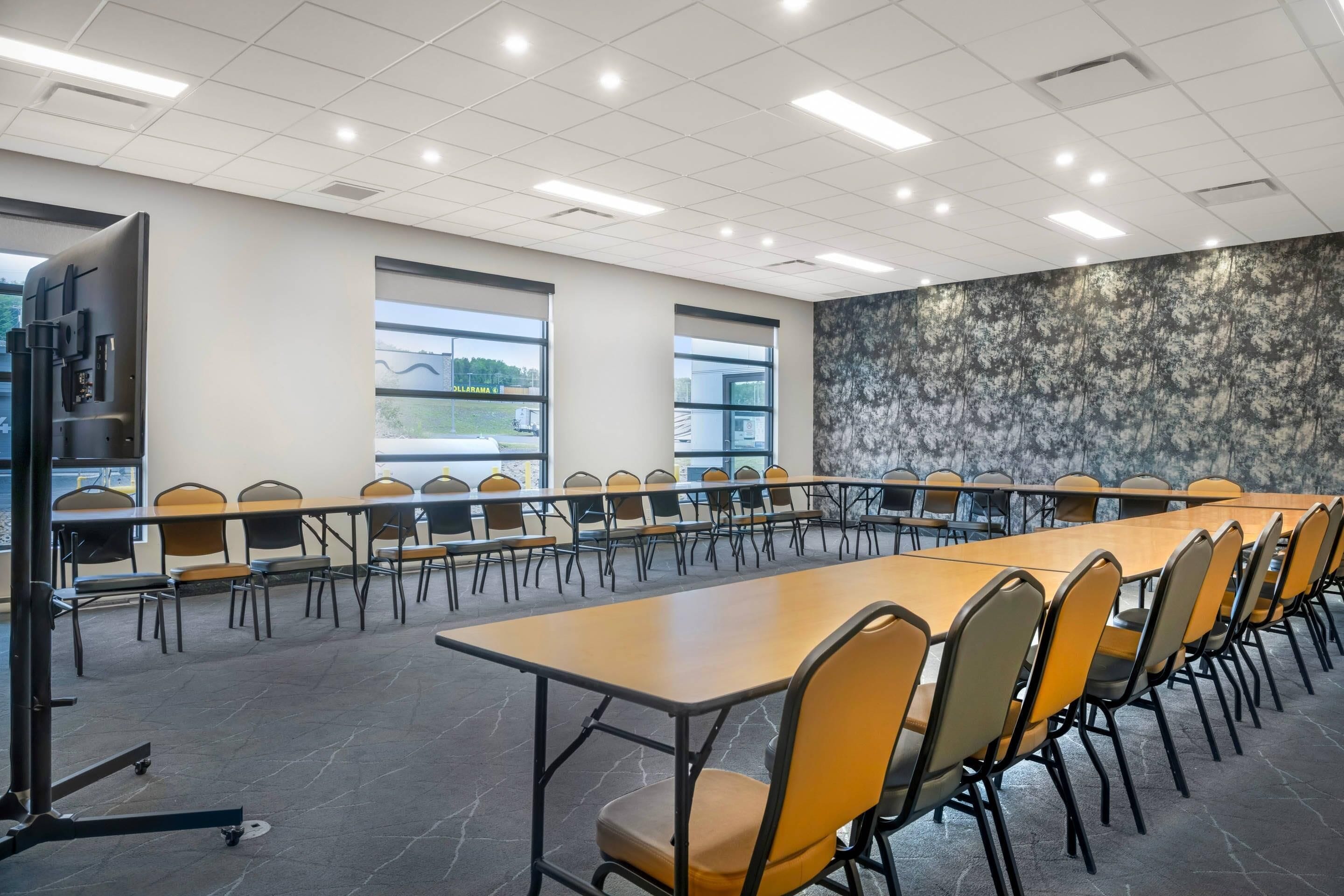 Une salle de conférence dotée de longues tables et de chaises, de grandes fenêtres et d’un mur à motifs.