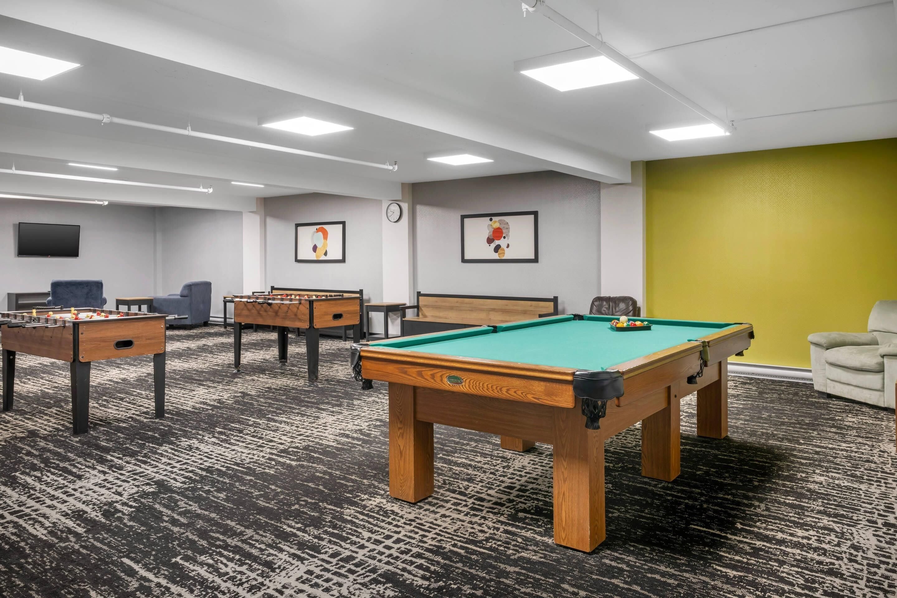 A recreational room with a pool table, foosball tables, and a television.