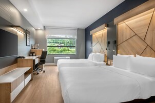 Habitación de hotel moderna con dos camas, un escritorio, una silla y un amplio ventanal con vista a zonas verdes.