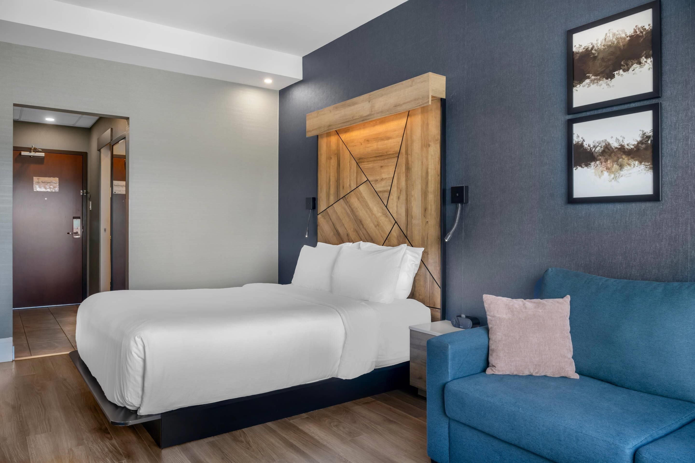 Una habitación de hotel moderna con una cama grande, un sofá azul y un cabecero de madera.