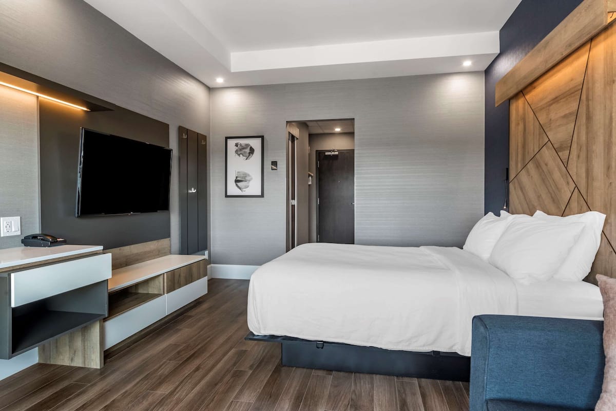 A modern hotel room with a large bed, built-in TV, and a desk with a chair.