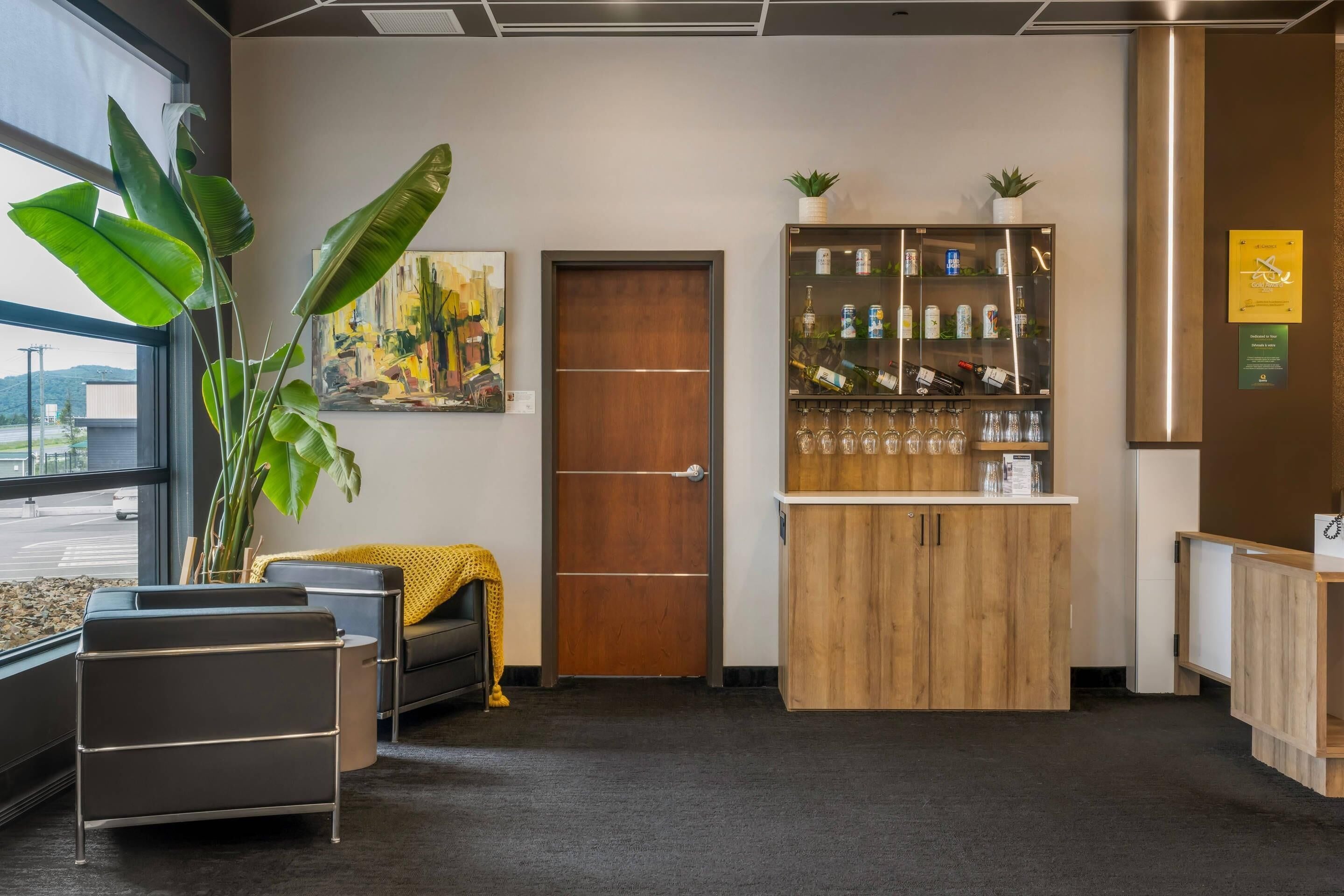 Een receptie met een houten kast met flessen en glazen, een grote plant en een schilderij aan de muur.