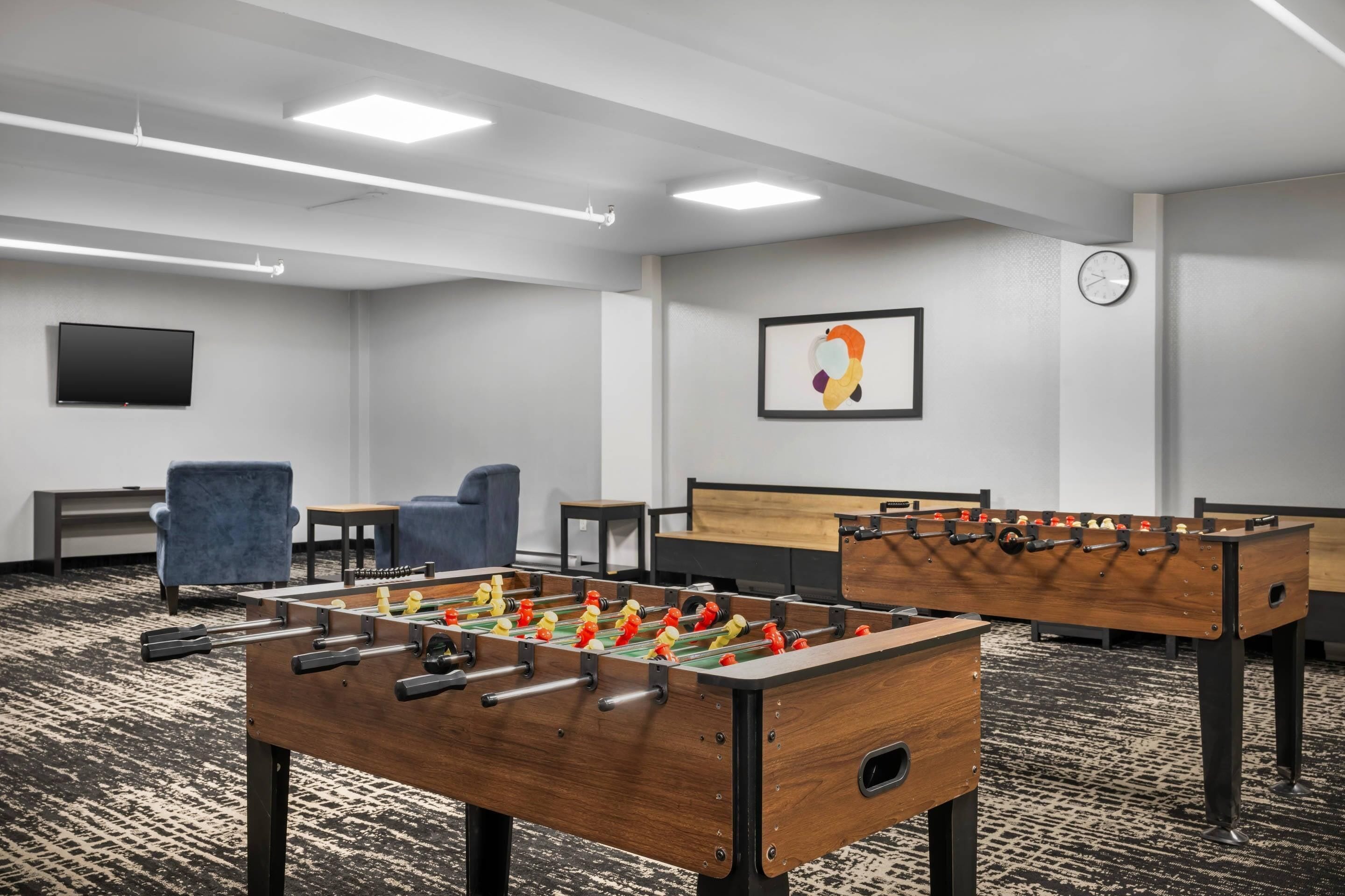 Une pièce équipée de deux tables de baby-foot, d’un téléviseur, d’une horloge et de plusieurs coins salon.