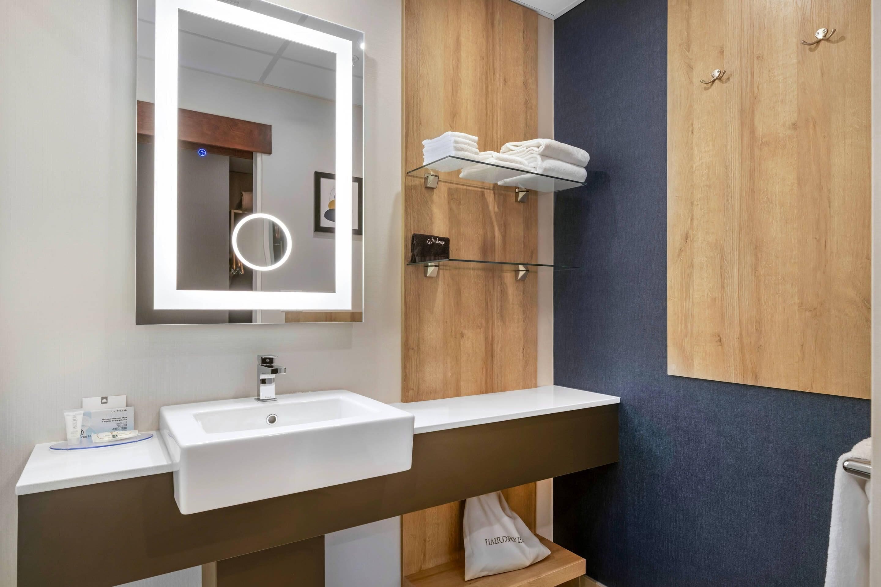 A modern bathroom with a large mirror, a white sink, and a towel rack.