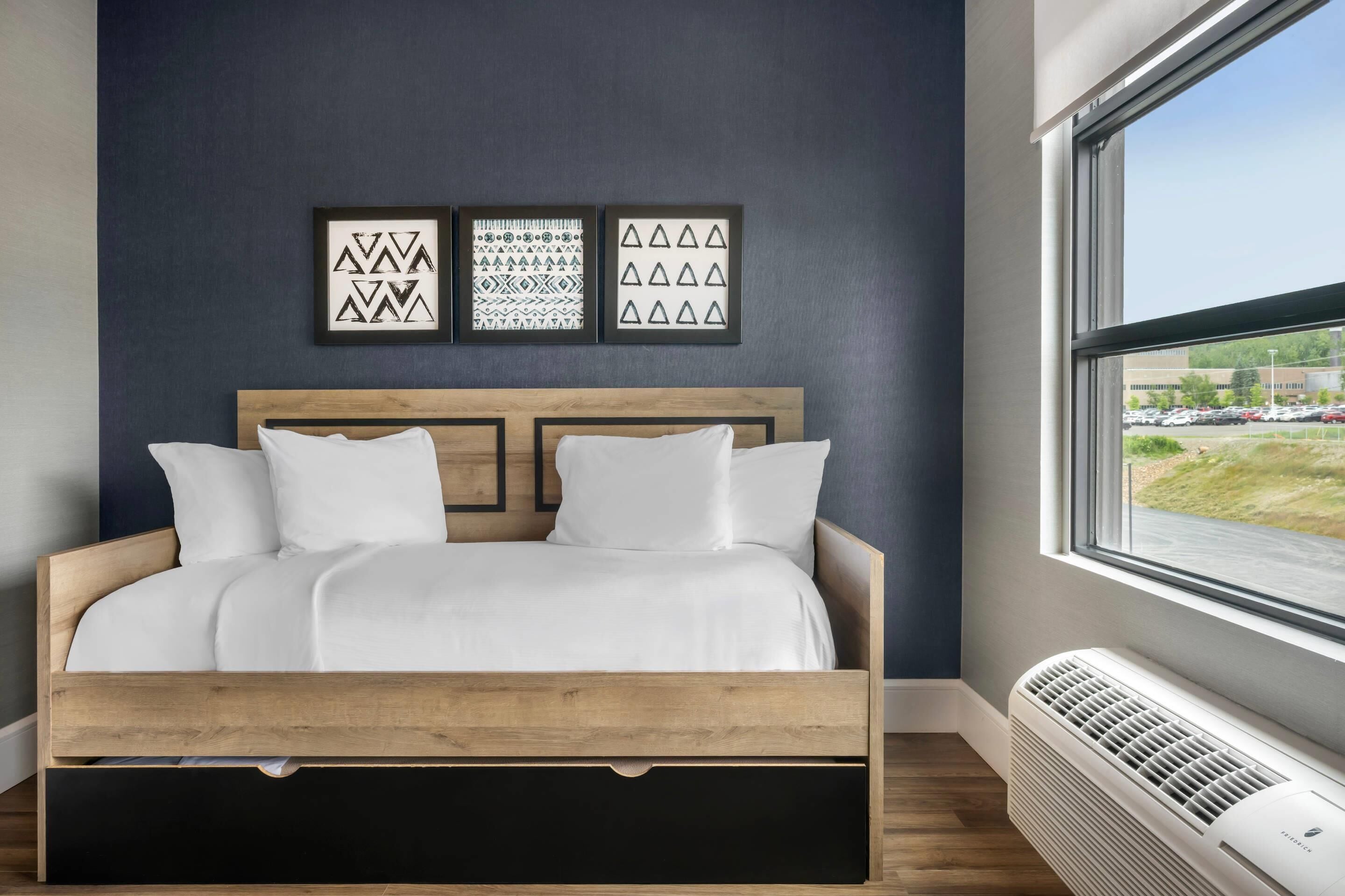 A bedroom with a wooden bed, white bedding, and three framed wall art pieces.