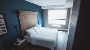 A bedroom with a bed, a nightstand, a wall-mounted shelf, a window, and a ceiling fan. - Quality Hotel & Conference Centre (Edmundston)