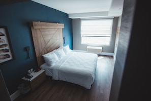 A bedroom with a bed, a nightstand, a wall-mounted shelf, a window, and a ceiling fan. - Quality Hotel & Conference Centre (Edmundston)