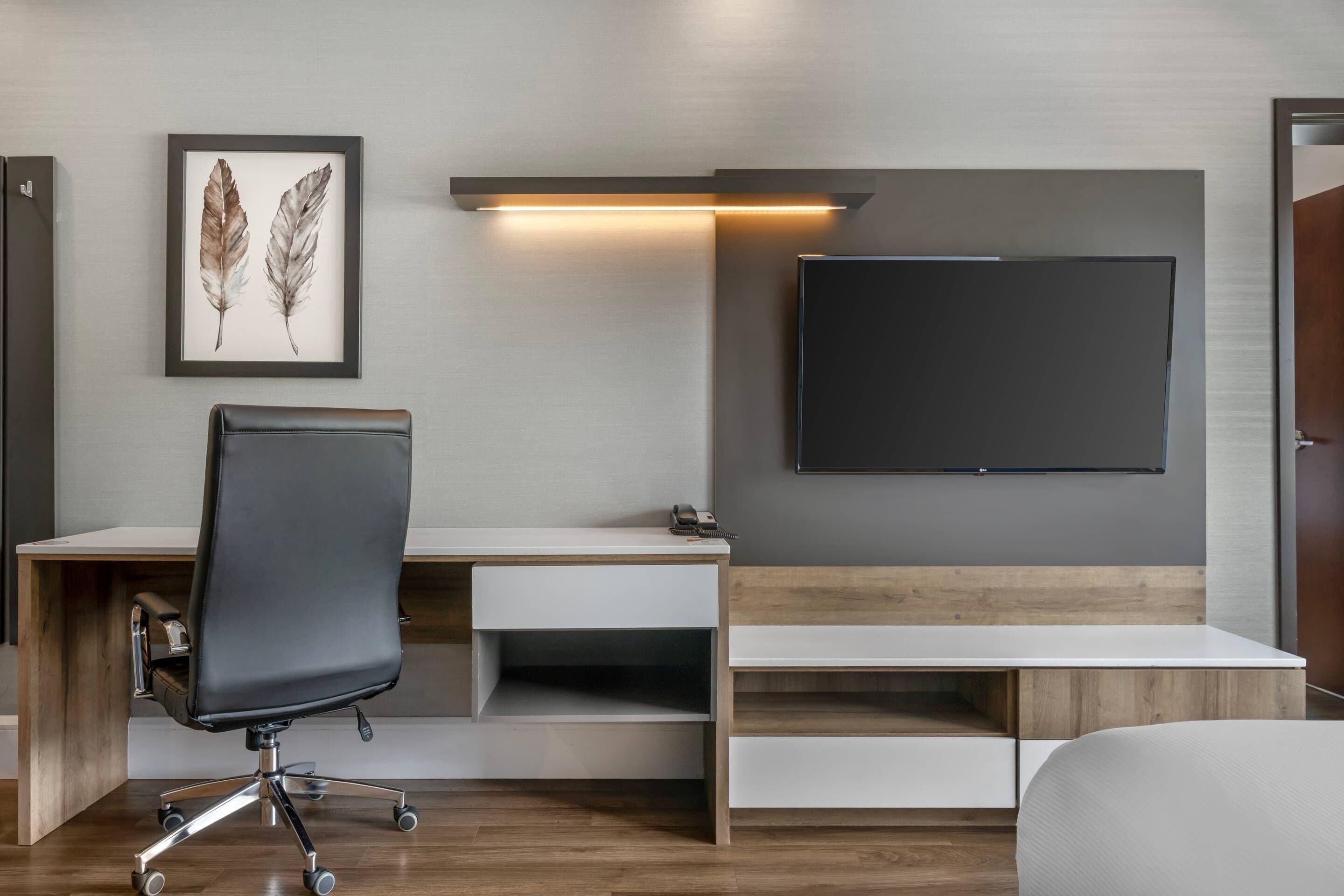 A modern hotel room with a desk, chair, and a mounted flat-screen TV.