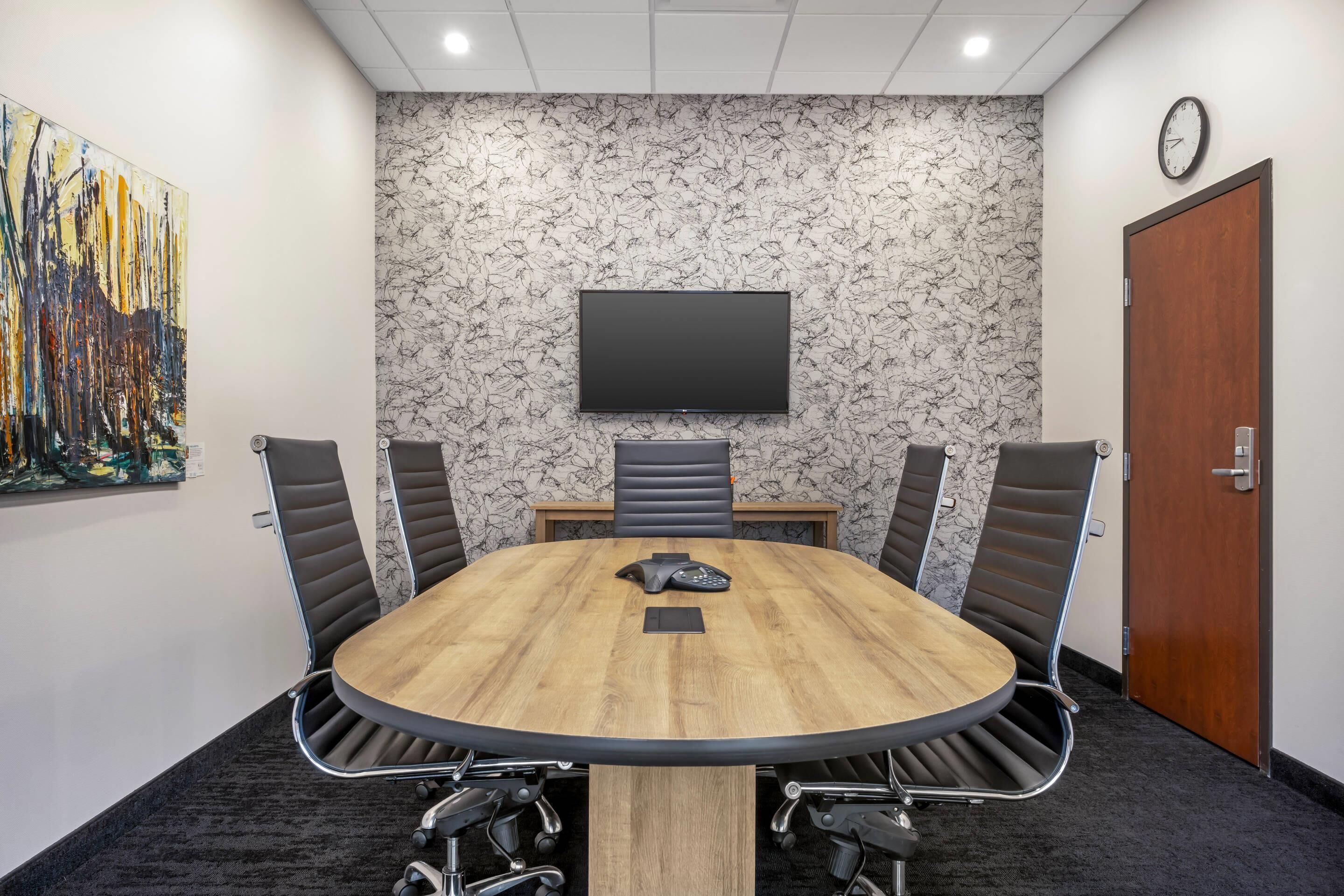 A conference room with a round table, four chairs, a flat-screen TV on the wall, and a door.