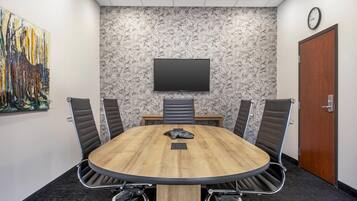 A conference room with a round table, four chairs, a flat-screen TV on the wall, and a door.
