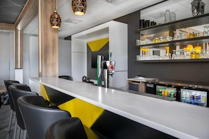 Zona de bar moderna con una barra larga, taburetes, un refrigerador lleno de bebidas y una variedad de copas en estantes.