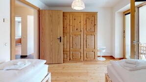 A hotel room with wooden flooring, a large wardrobe, a bed with white bedding, a small white table, and a hanging light fixture. - The spacious 3 room apartment is located in a multi - family house at the villag (Celerina/Schlarigna)