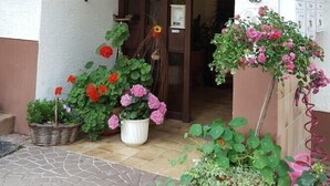 Ett trästaket med klätterväxter, en dörr med en hängande krans och krukväxter med blommor.