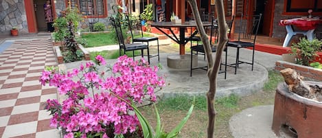 Un patio con suelo a cuadros, una mesa con sillas y flores rosas.