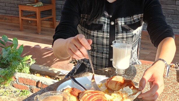 Una persona sentada a una mesa con un plato de comida, un vaso de leche y una planta colgante.