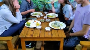 Un grupo de personas sentadas alrededor de una mesa de madera con platos de comida, tazones y cubiertos.