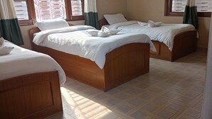 Habitación de hotel con dos camas de madera, cada una con ropa blanca y almohadas, y suelo de baldosas.