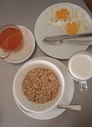 A breakfast setting with a plate of eggs, a bowl of granola, a glass of tea, and a mug of coffee. - Pokhara Metro Eco Hotel - Hostel (Pokhara)