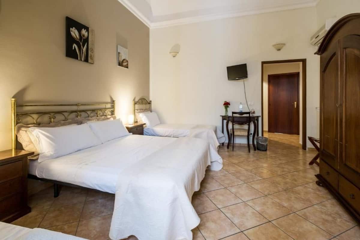 A hotel room with two beds, a TV, a small table with flowers, and a wardrobe.