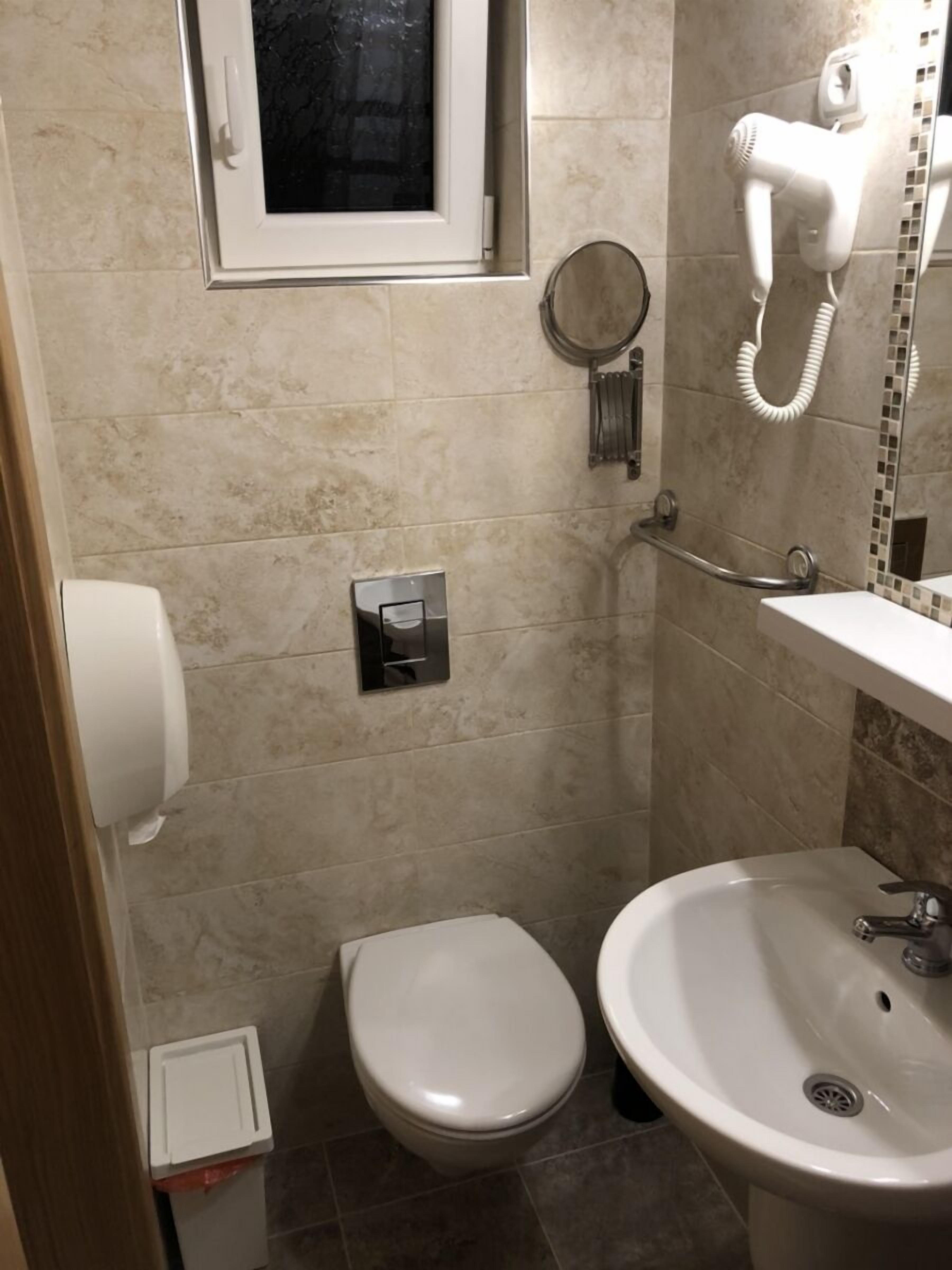 A small bathroom with a toilet, sink, and a hairdryer mounted on the wall.