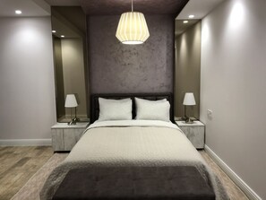 Une chambre moderne avec un grand lit, deux tables de chevet avec des lampes, un luminaire suspendu et un miroir au mur.
