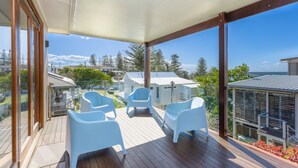 Una terraza exterior cubierta con dos sillas blancas, suelo de madera y vistas a casas y árboles.