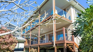 A modern two-story house with a balcony, a visible window, and a clear sky.
