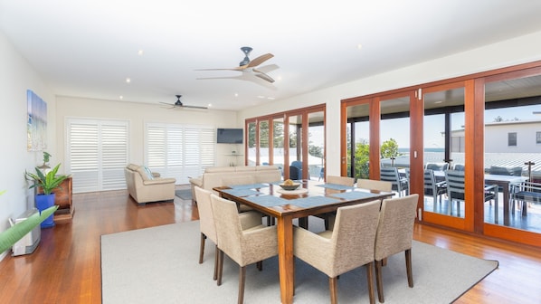 A spacious living area with a dining table, sofas, and a ceiling fan.
