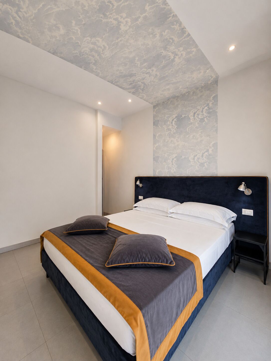 Un dormitorio moderno con una cama, mesitas de noche y un techo con diseño de nubes.