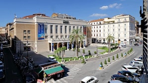 Una calle urbana con un edificio de teatro, coches aparcados y palmeras.