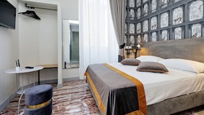 Una habitación de hotel con una cama grande, una mesita, una silla, un televisor y una pared con un mural.