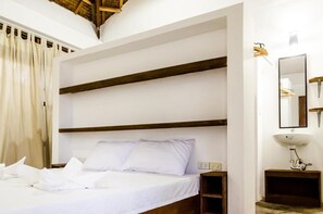 A hotel room with a large bed, wooden headboard, a bedside table, a mirror, and a white sink. - Blauset House Ii (General Luna)
