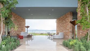 A modern outdoor living area with a view of the landscape, featuring a stone wall, a white sofa, and a red chair. - Gamma Monterrey Rincón de Santiago. (Santiago)