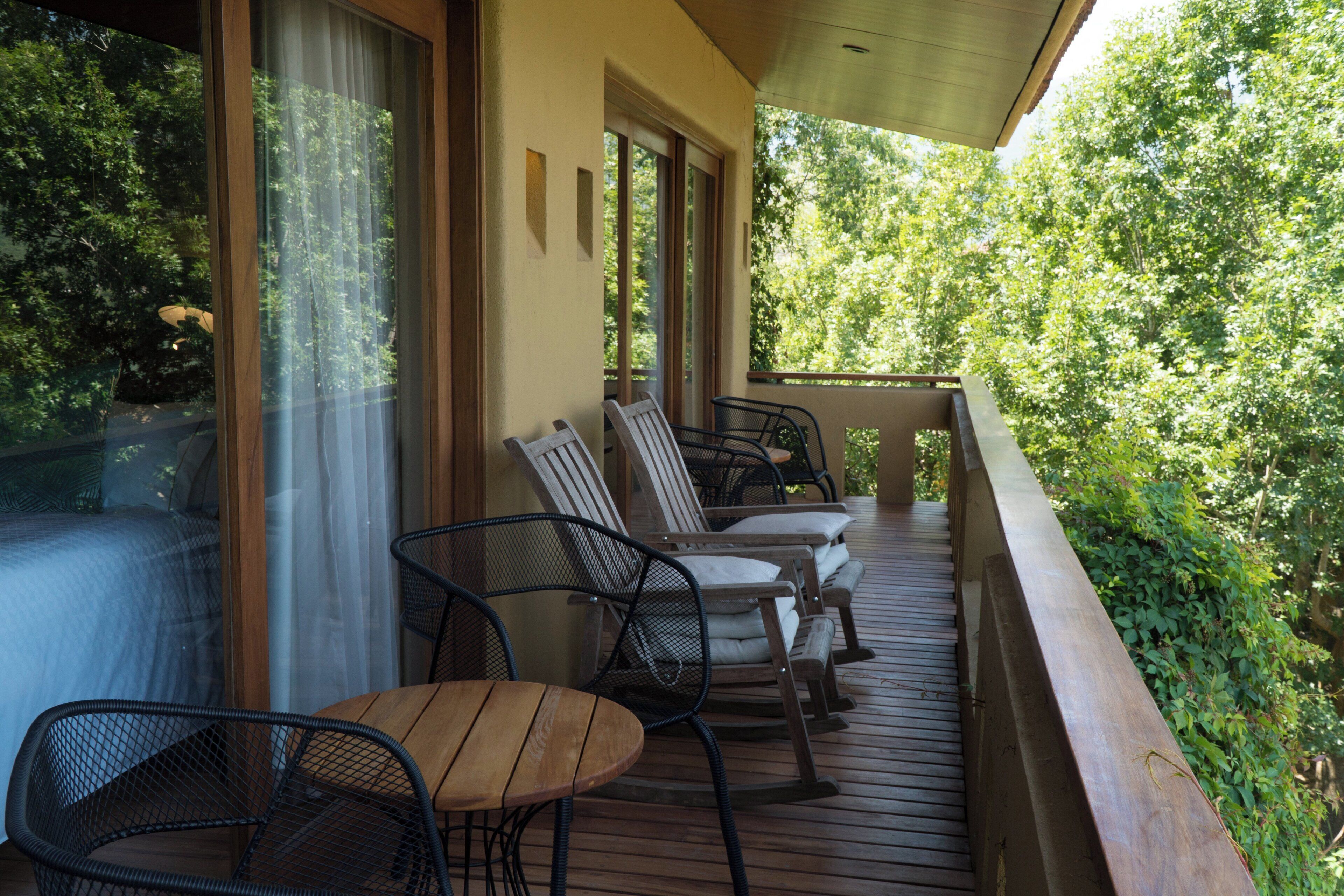 A wooden deck with outdoor seating, large windows, and a view of lush greenery.