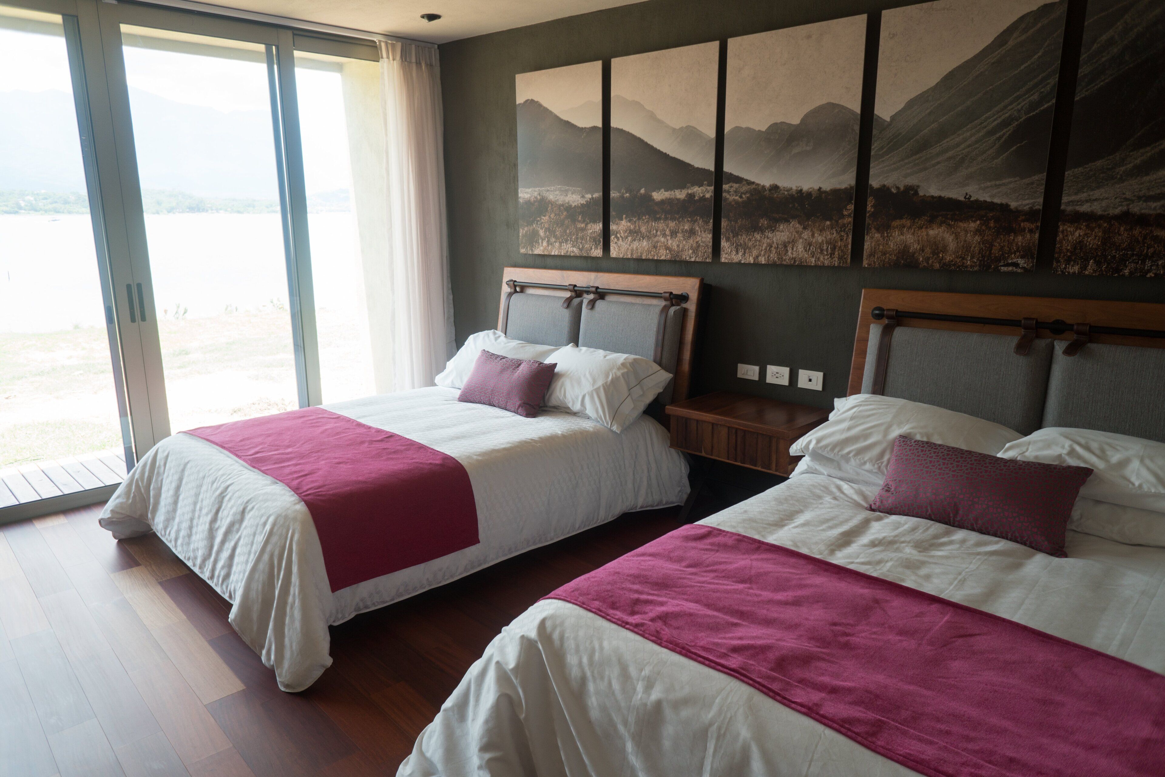 Ein Hotelzimmer mit zwei Betten, einem großen Fenster und einem Wandbild mit Berglandschaft.