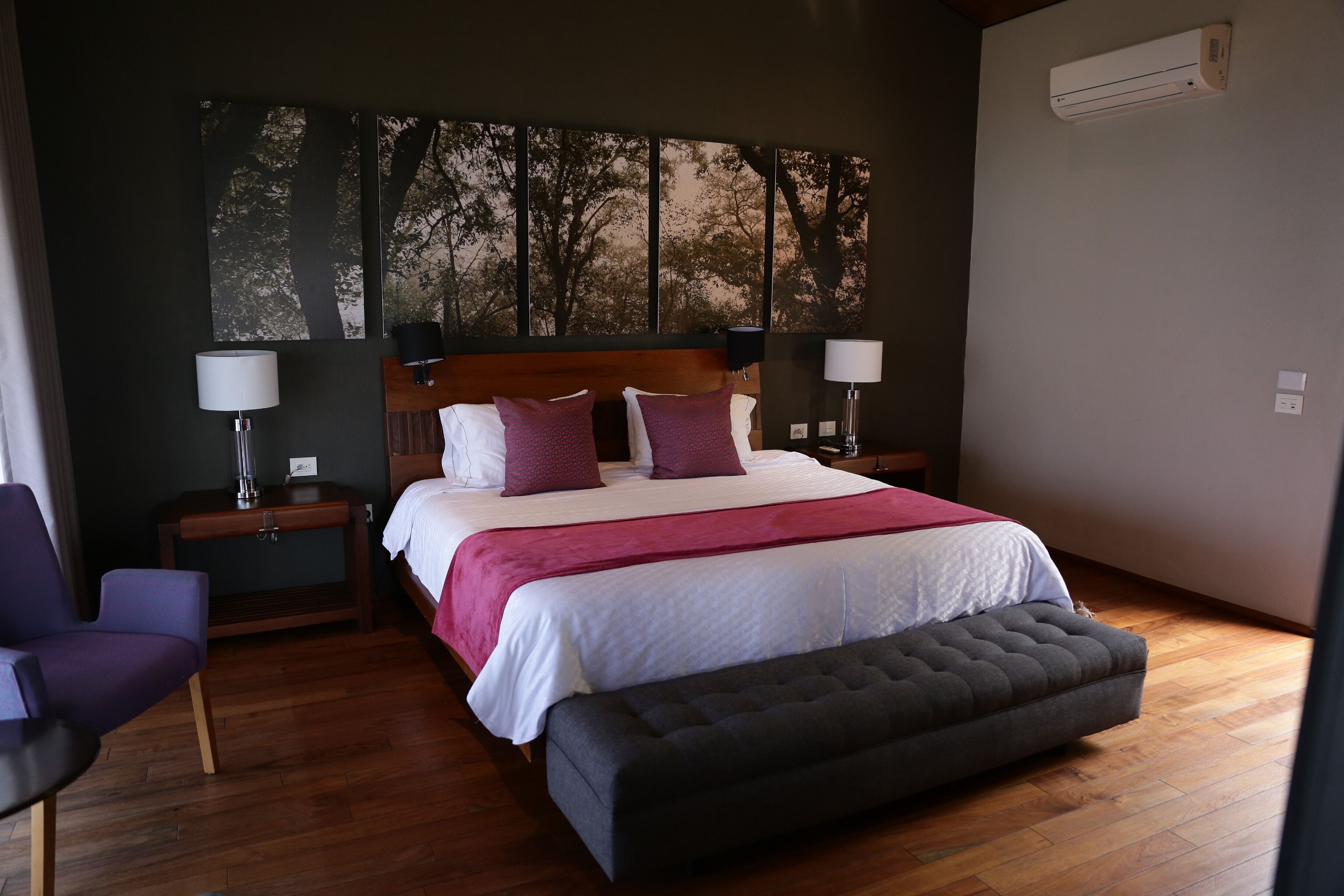 Ein Schlafzimmer mit einem großen Bett, zwei Nachttischen, einer Bank und einer Wand-Klimaanlage.
