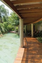 Un paseo techado con piscina, rodeado de follaje y columnas.