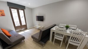 Un salon moderne avec un canapé gris, une table à manger avec des chaises blanches et un téléviseur à écran plat fixé au mur.